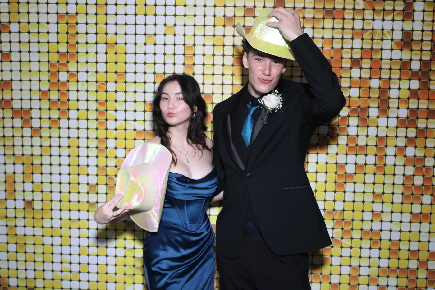 A couple in formalwear with novelty hats at the prom photo booth