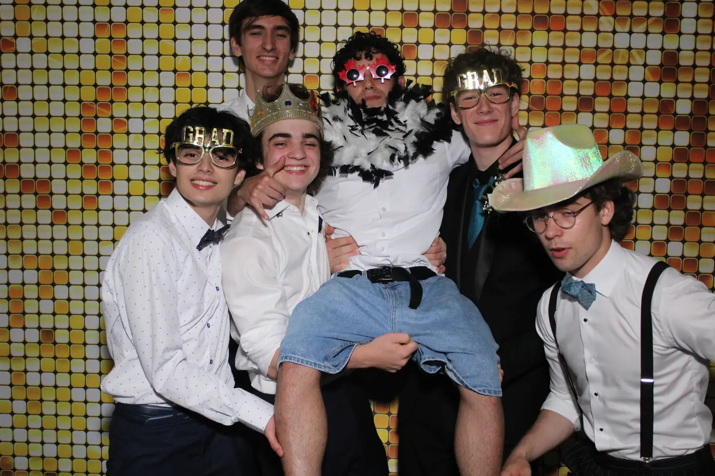 A group of graduates in grad glasses lifting a friend at the prom photo booth