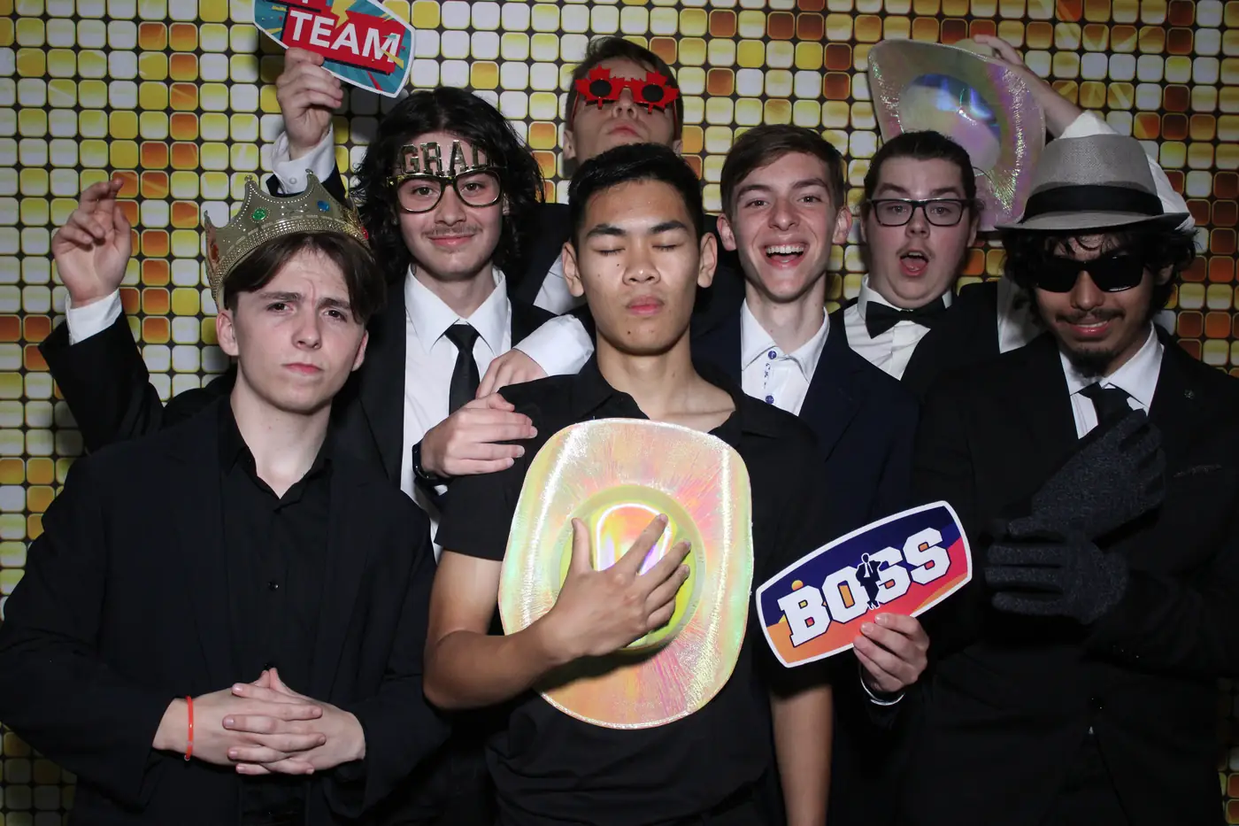 Prom guests in suits crowded into the photo booth with props