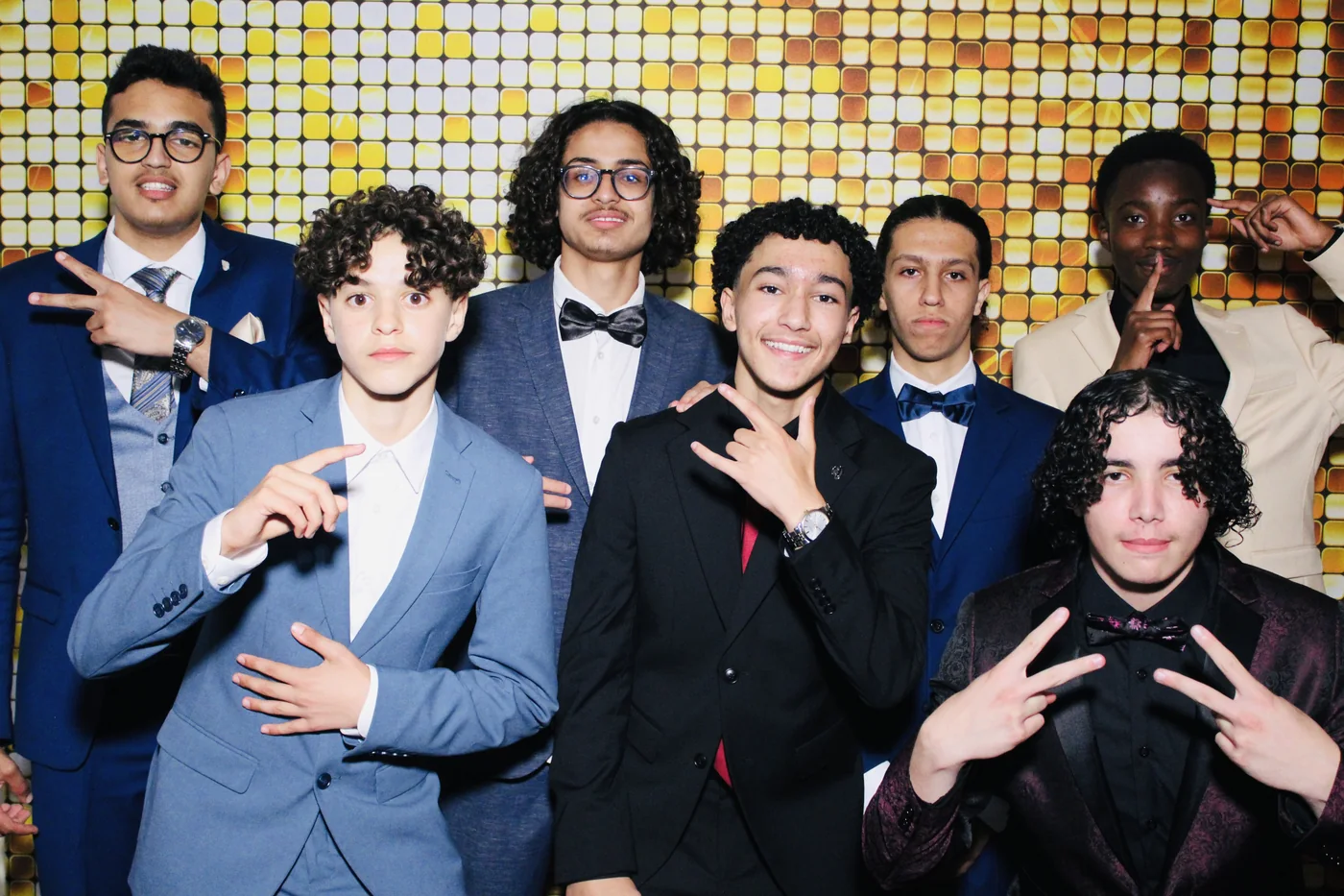 Members of a quinceañera court in suits posing with props against a gold backdrop