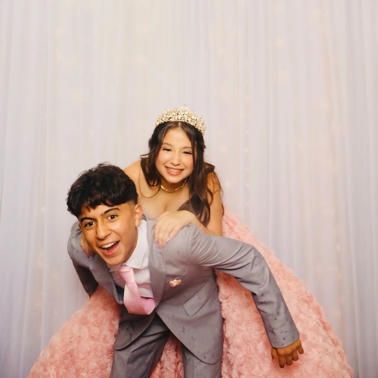 Quinceañera in a pink gown laughing while riding on a friend’s back at a Miami photo booth