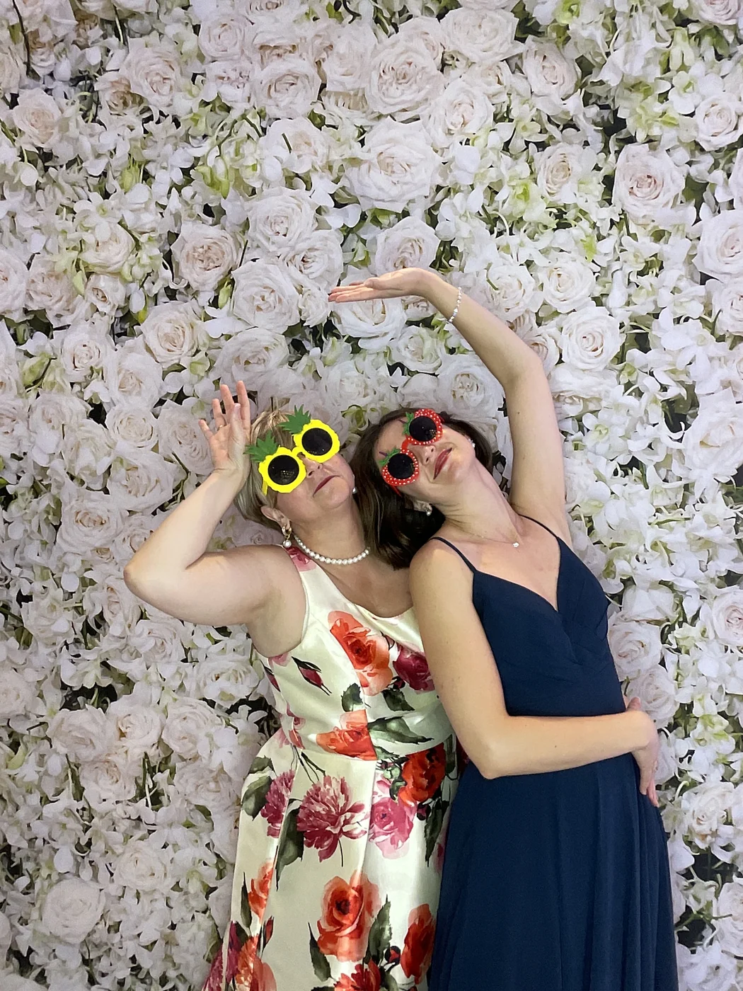 Two guests posing at the photo booth with a floral backdrop at a wedding in Aventura