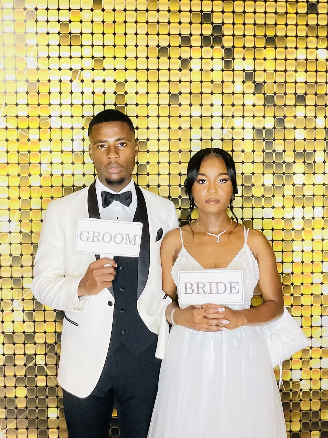 Bride and groom with signs at the photo booth against a gold sequin backdrop