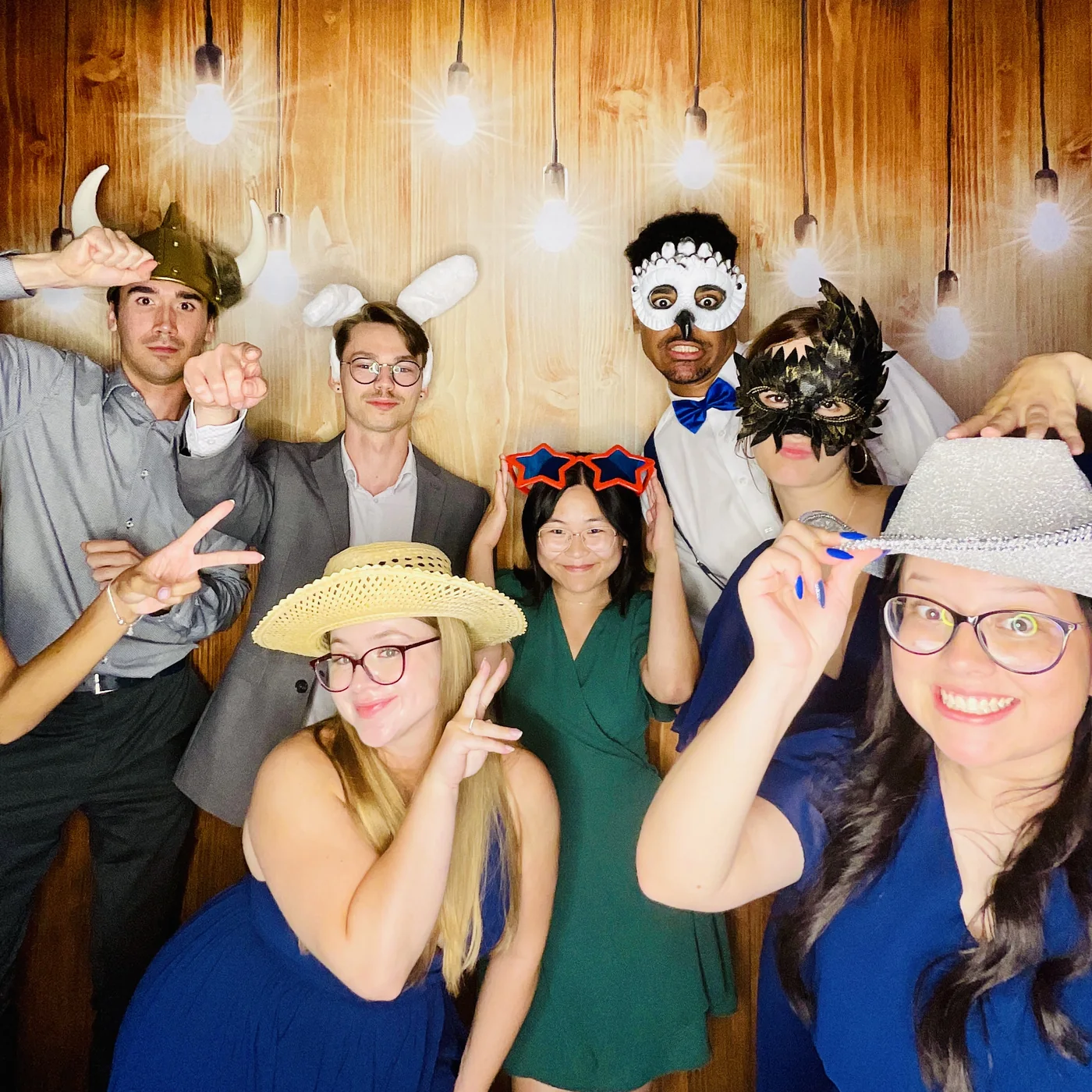 Guests in masks and props at the photo booth against a wood backdrop
